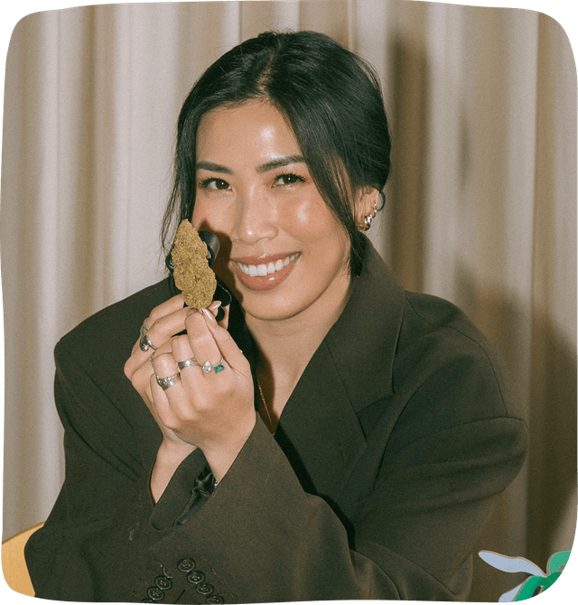 Anna the Cannabinista holding up a large cannabis nugget with a magnifying class held closely to it as she smiles at the camera.